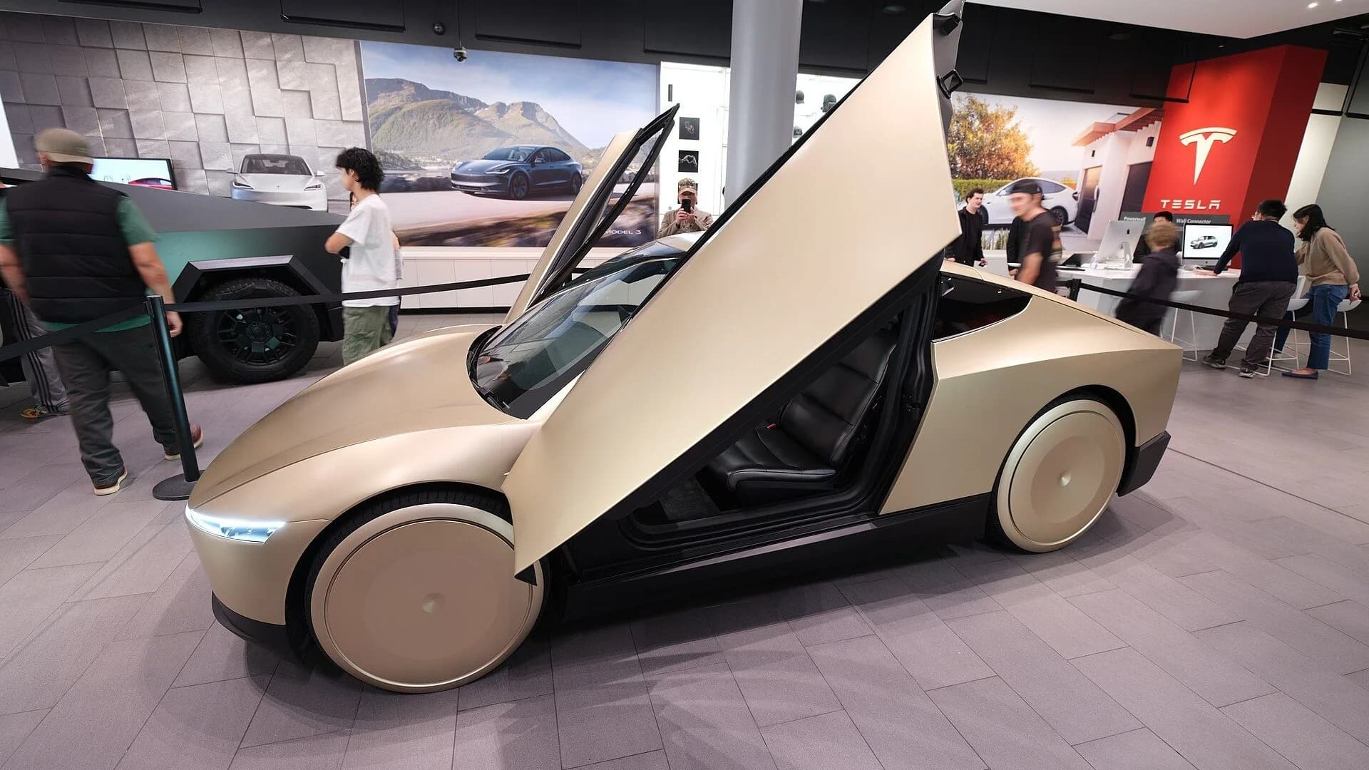 A gold Tesla Cybercab prototype with raised butterfly doors displayed in a Tesla showroom.