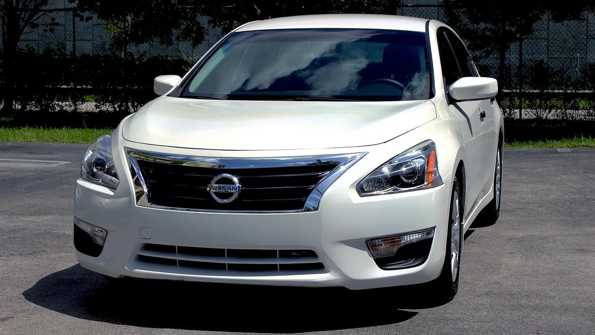 White Nissan sedan parked on asphalt, facing forward with a chrome grille and headlights visible.