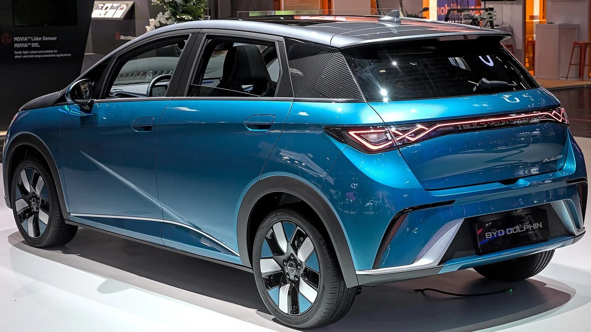 Rear three-quarter view of a blue BYD Dolphin electric hatchback on an auto show floor.