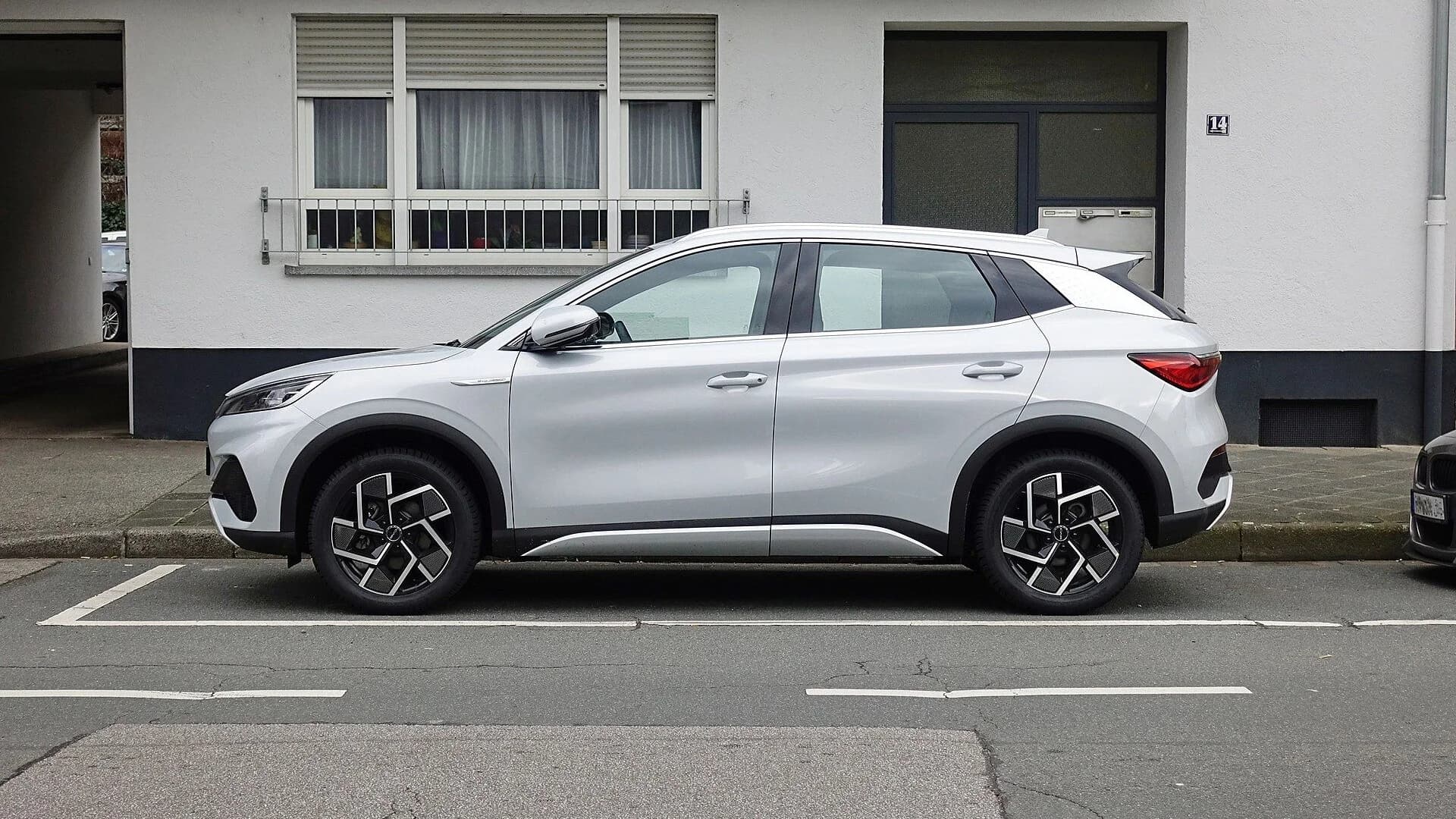 A silver BYD Atto 3 compact crossover EV parked on a city street in profile view.