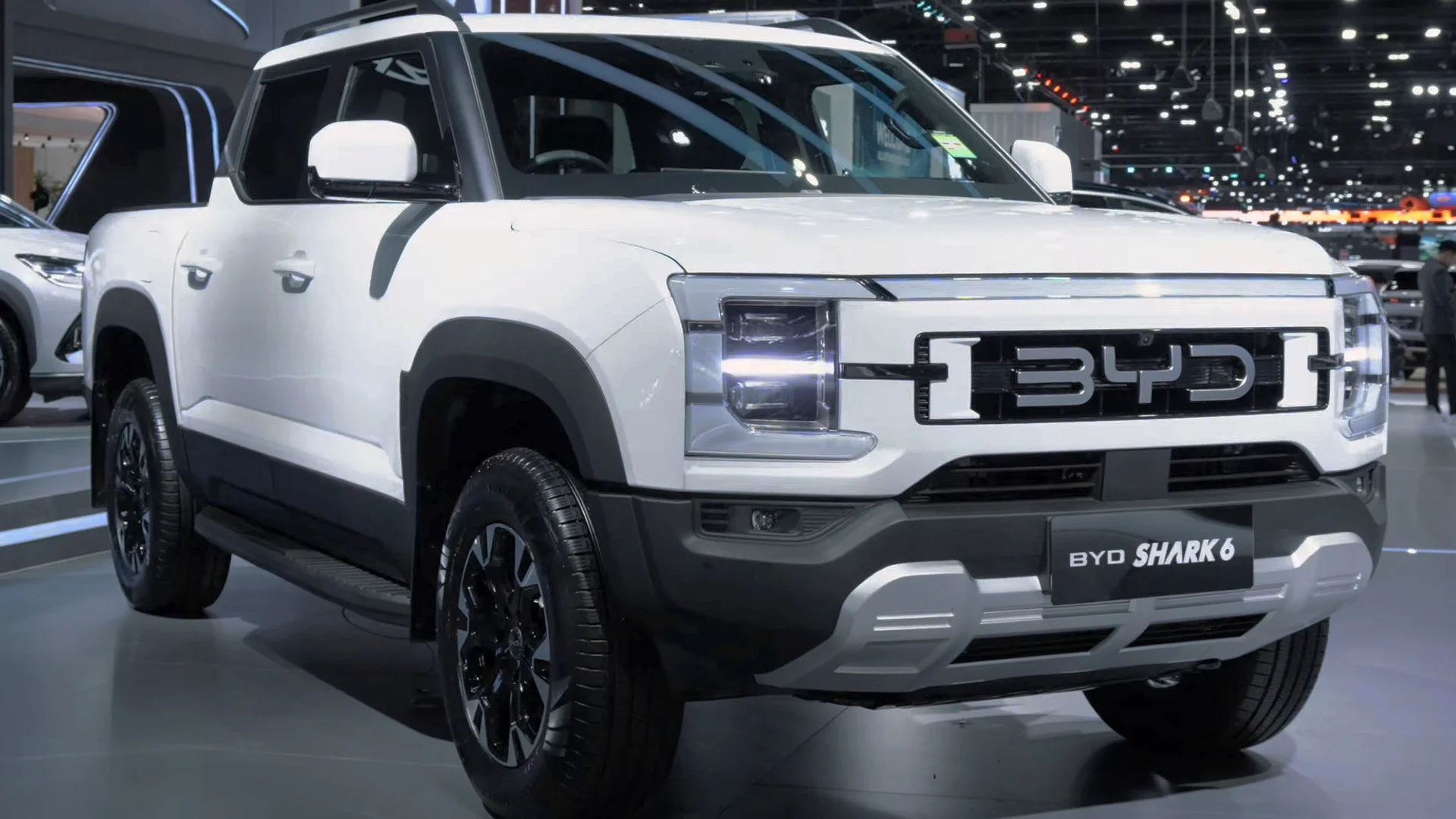 A white BYD Shark 6 pickup truck showcased on an indoor showroom floor.