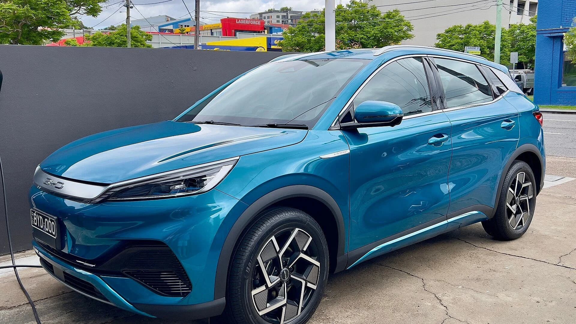 A blue BYD Atto 3 electric SUV parked on concrete next to a wall.