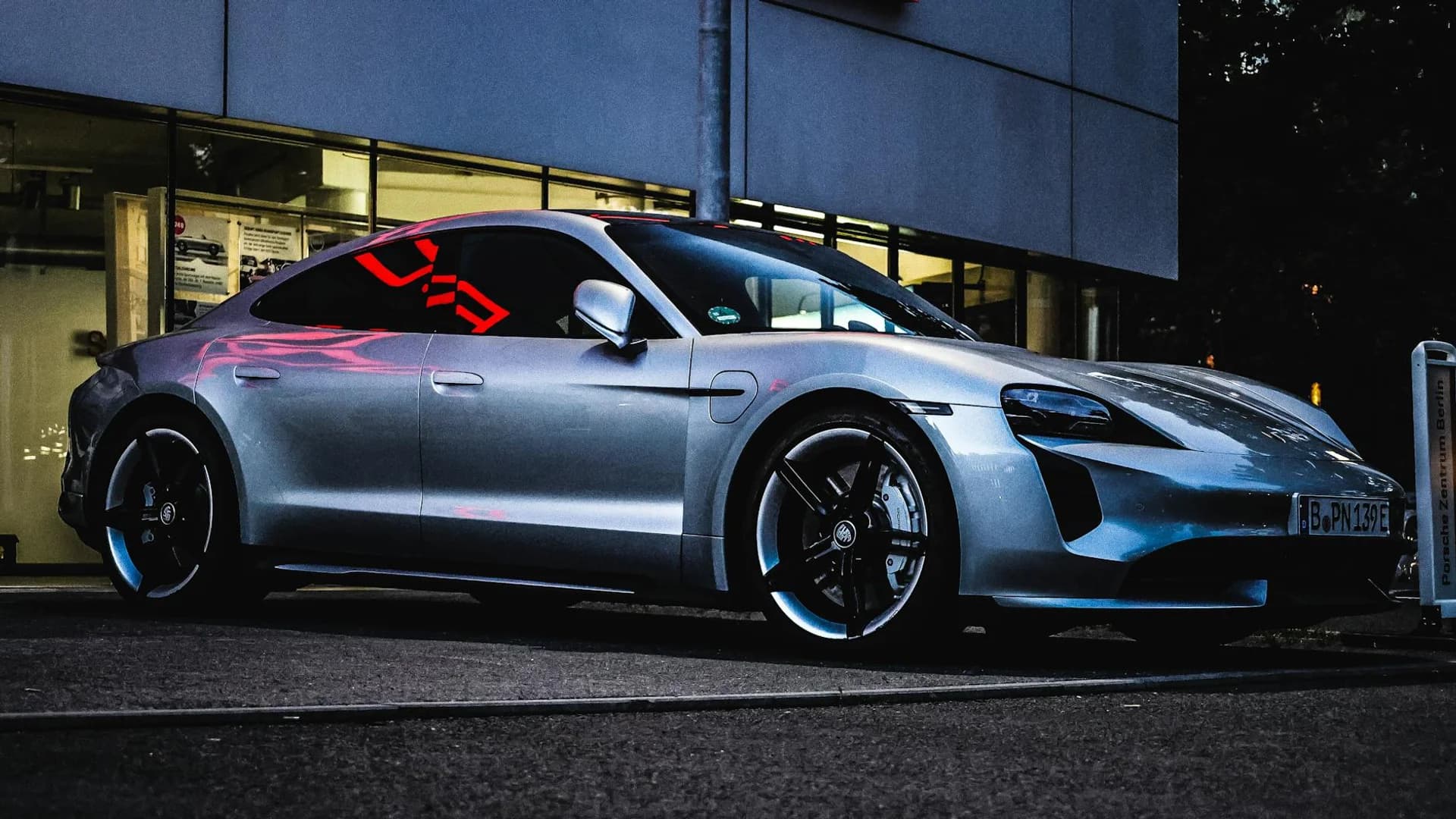 A luxurious silver sports car parked outside a modern building in Berlin, Germany at twilight.