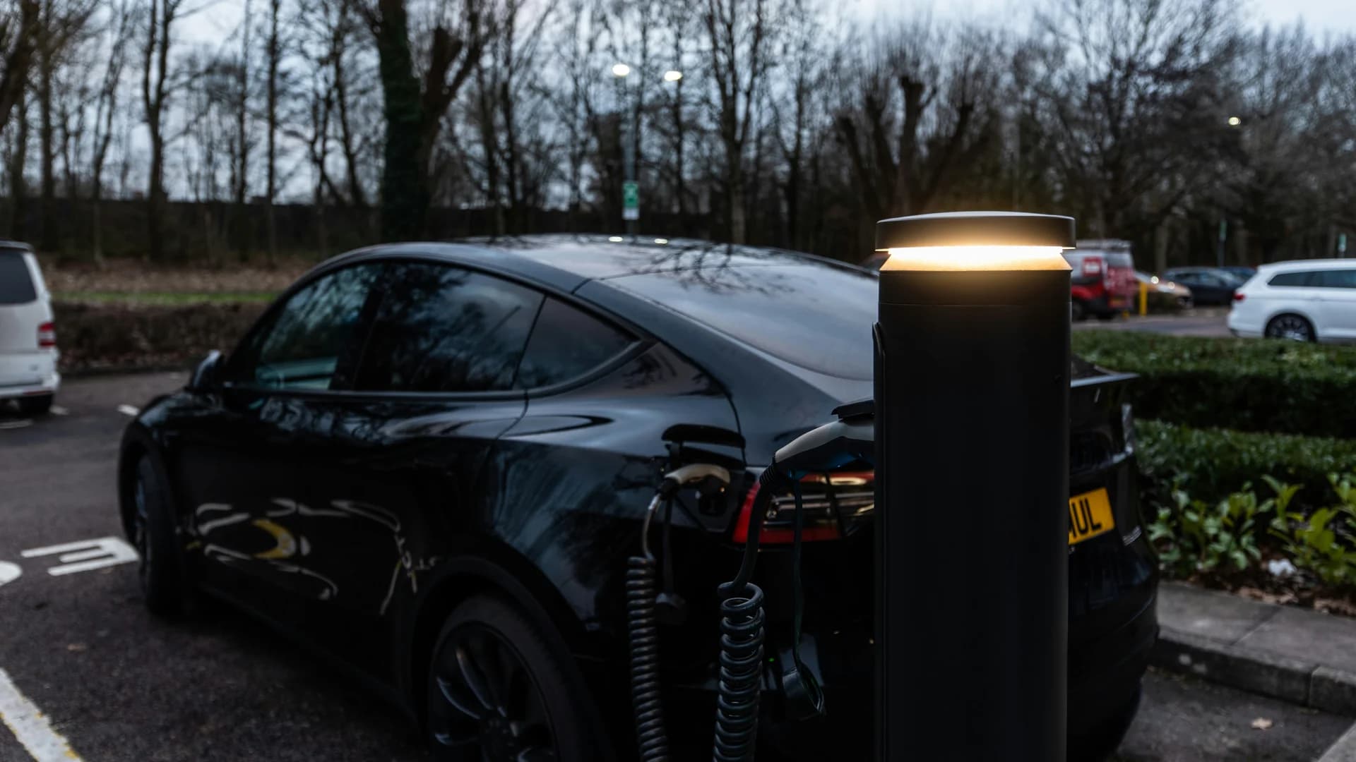 Black electric car charging at an outdoor station.