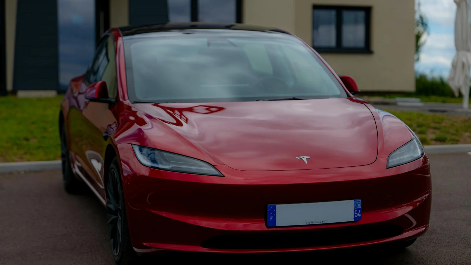 A red Tesla car with a black roof is parked on asphalt, facing forward.