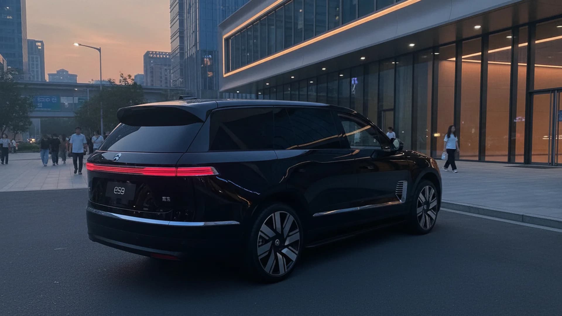 Rear side view of a black NIO ES9 SUV parked outside a modern glass building at dusk