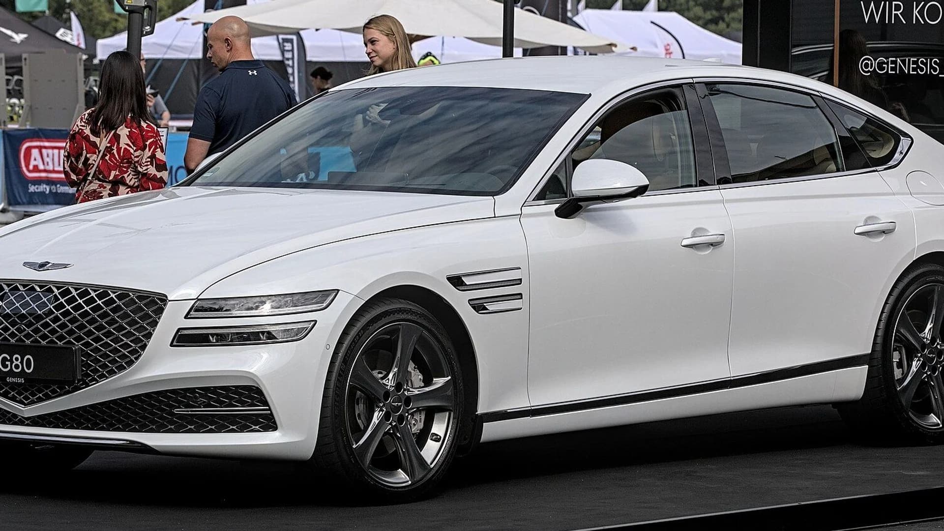A sleek white Genesis G80 sedan parked on display at an outdoor event.