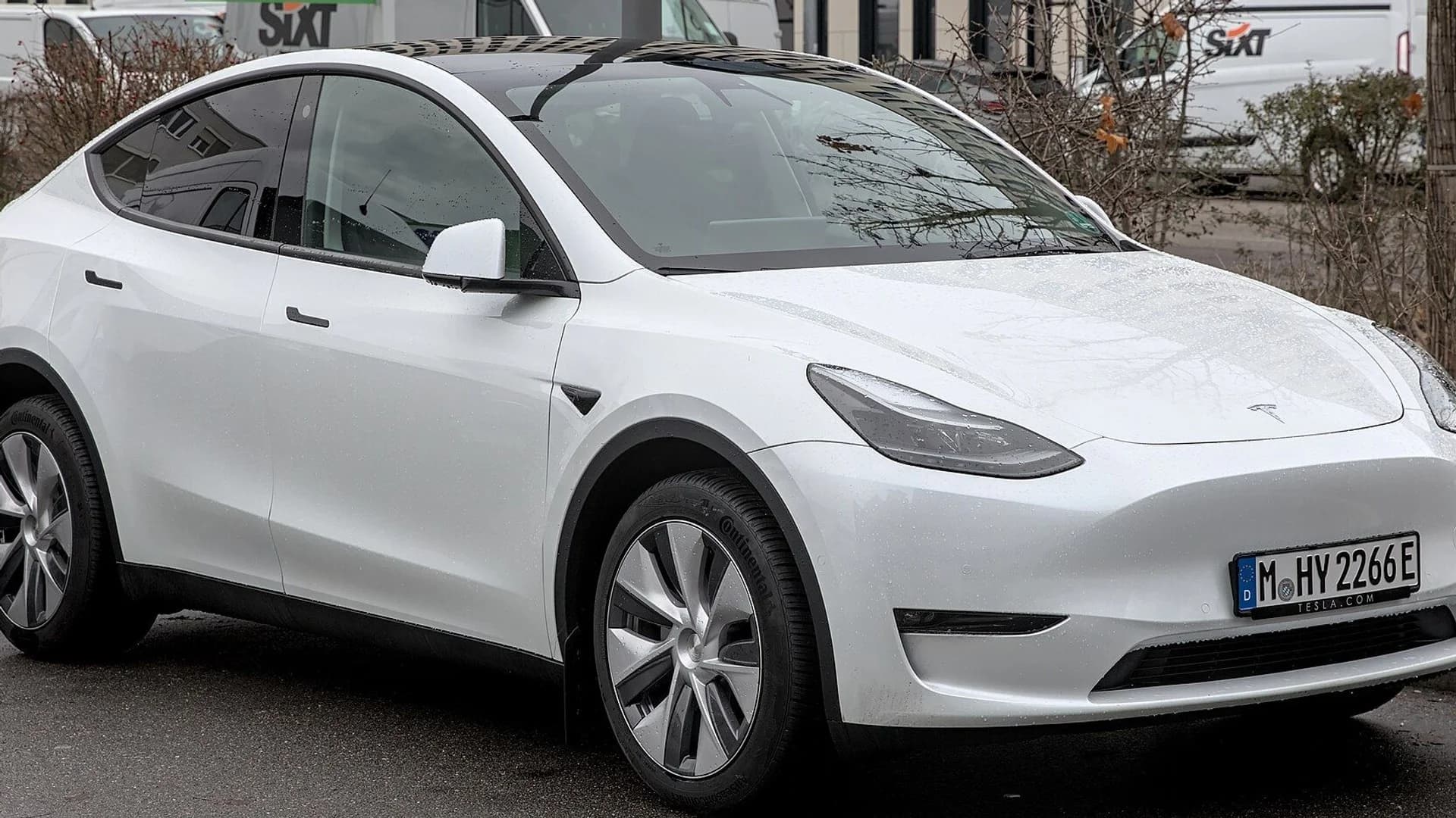 A white Tesla Model Y parked on an asphalt street with buildings in the background.