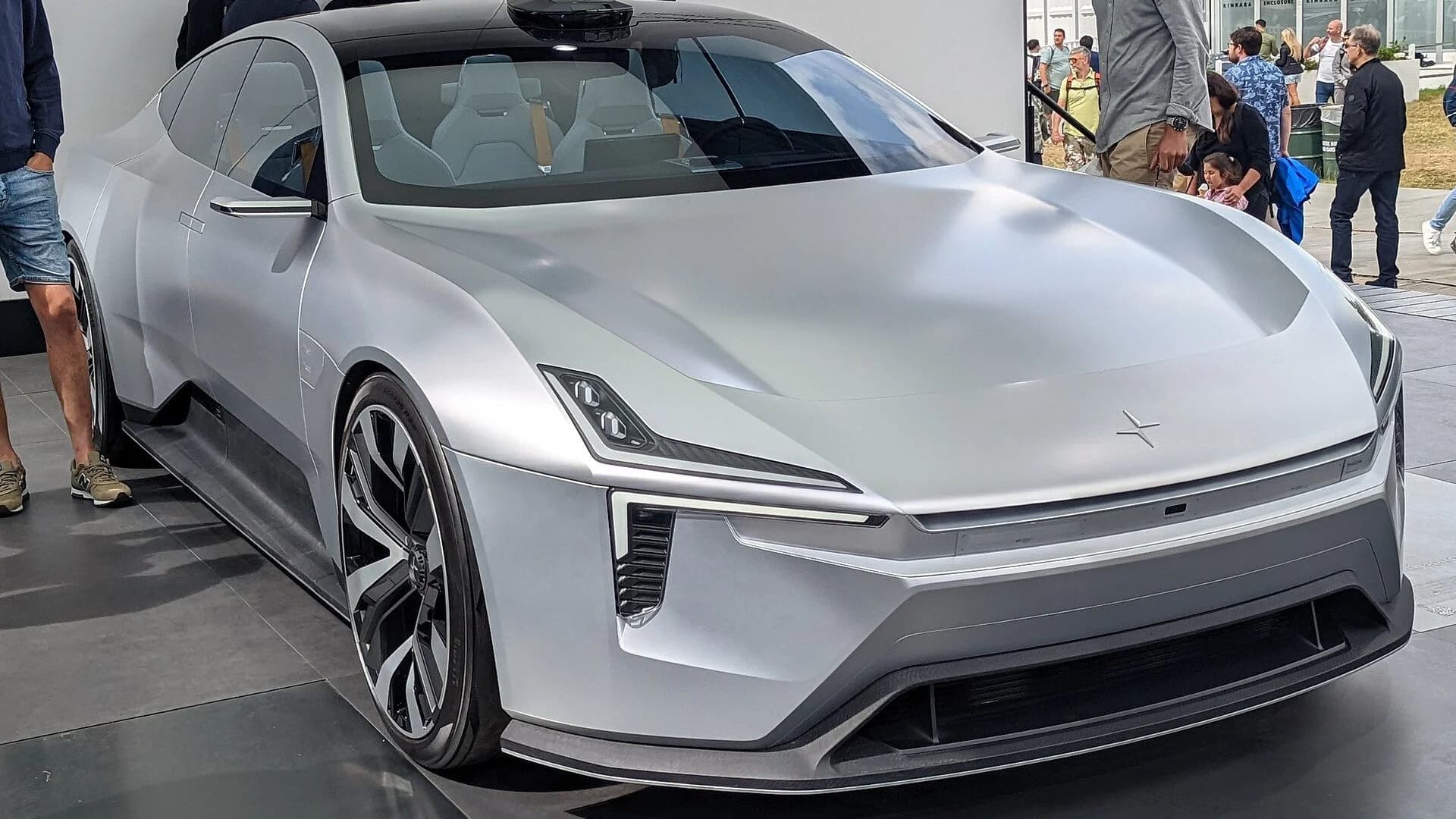 Silver futuristic Polestar concept sedan on display with visitors blurred in the background.