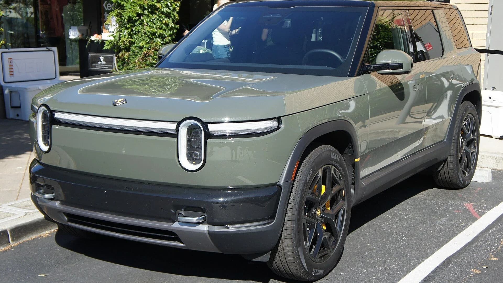 A sage green Rivian R2 electric SUV parked in a sunlit lot.