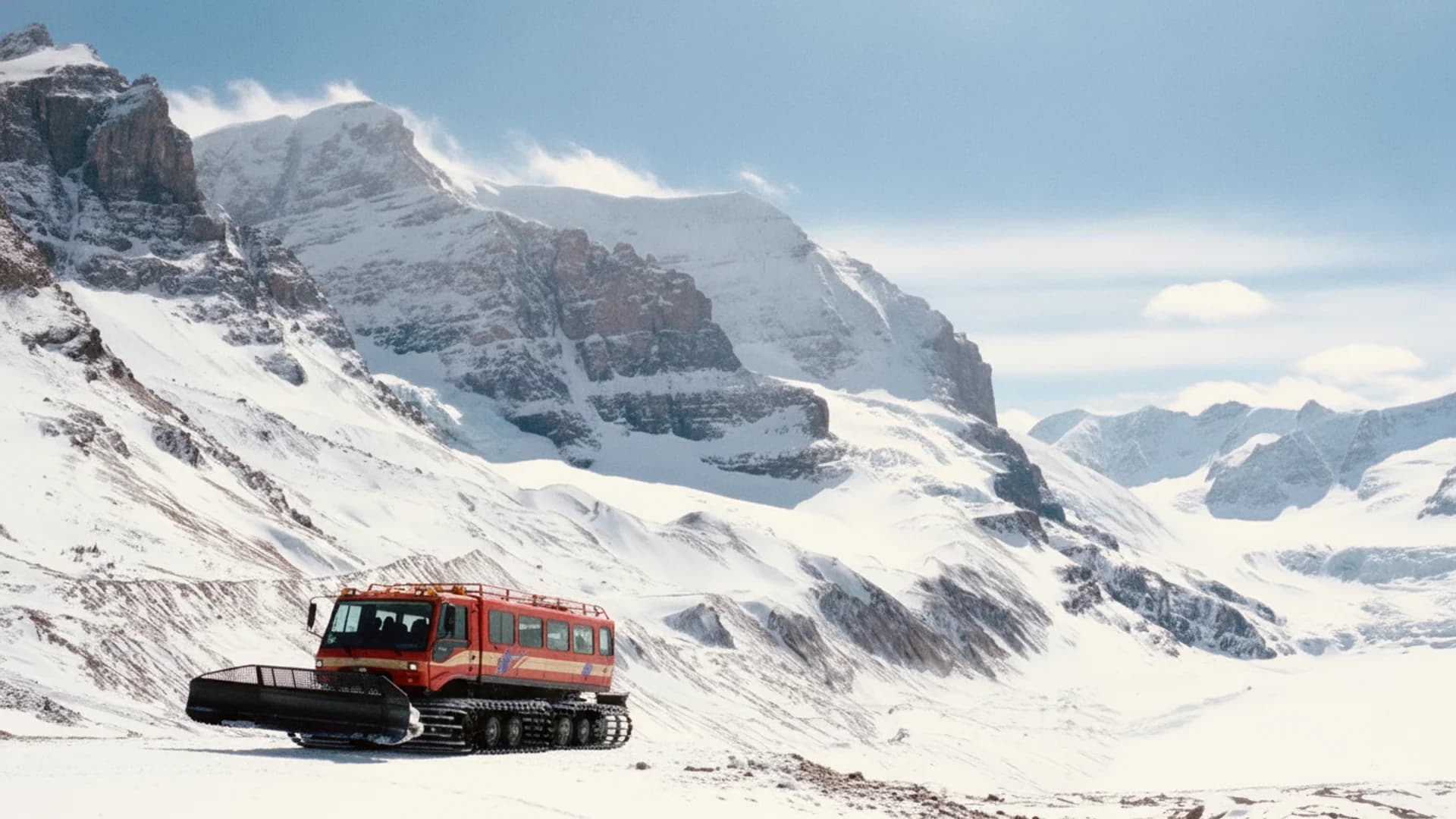 A red snow coach parked in a snowy mountain landscape on the Athabasca Glacier under bright skies.