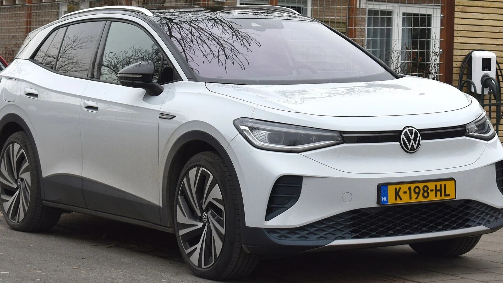 A white Volkswagen ID.4 electric SUV parked on a paved street near a charging station.