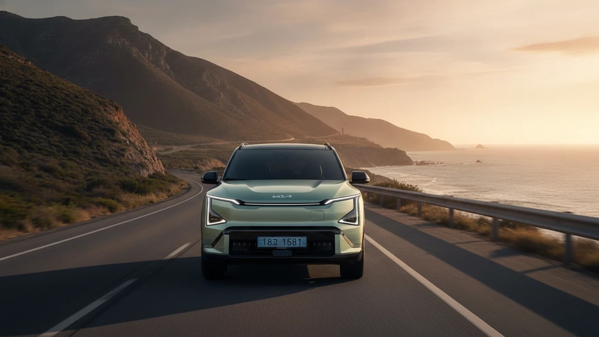 A light green Kia car drives on a coastal road with mountains on the left and the ocean on the right.