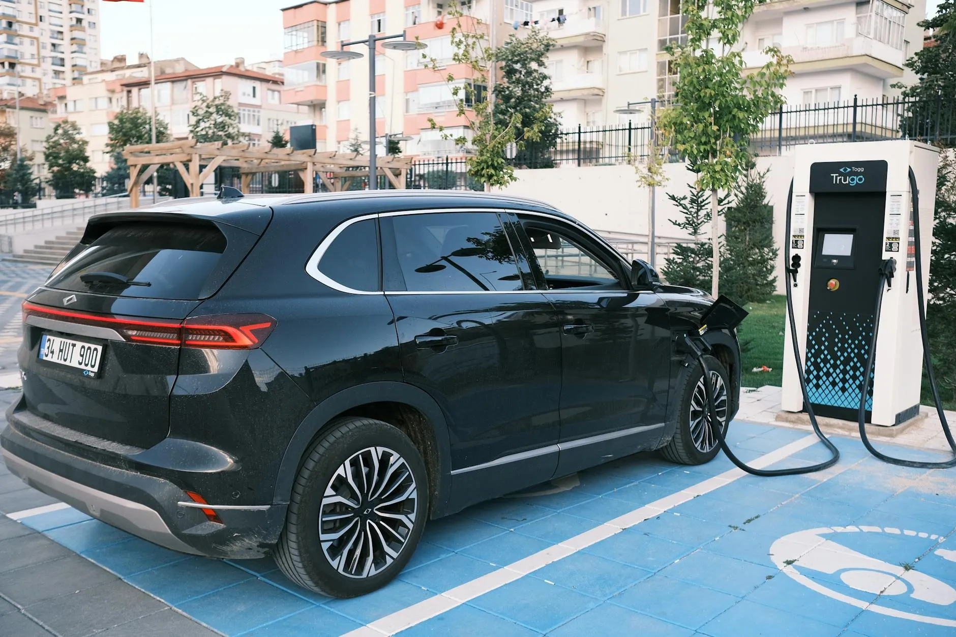 Close-up of a person plugging in an electric car at a charging station outdoors.