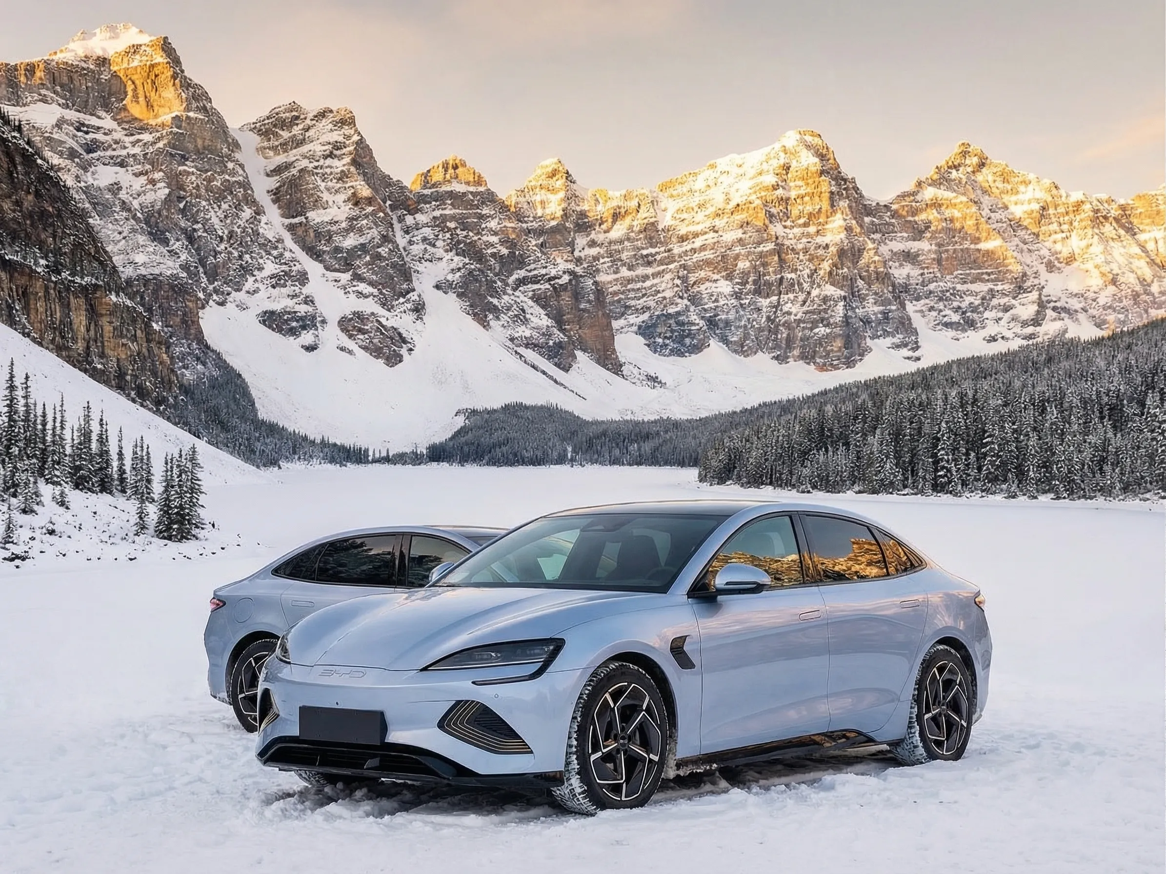 Blue BYD Seal electric sedan at a scenic Canadian lakeside viewpoint with Rocky Mountains and snow-capped peaks in golden hour light
