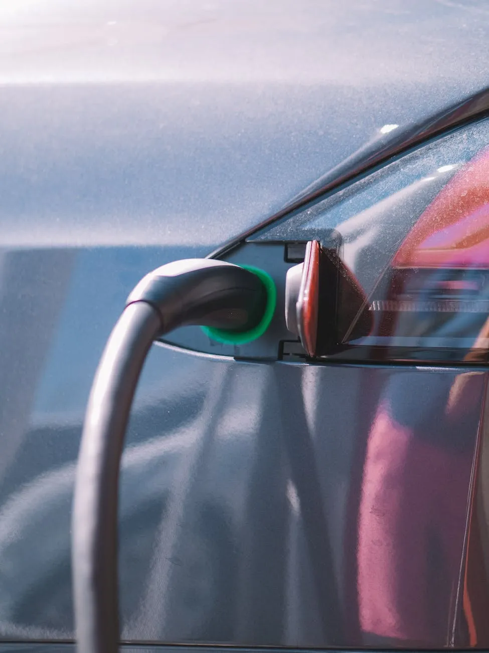 Close-up of a person plugging in an electric car at a charging station outdoors.